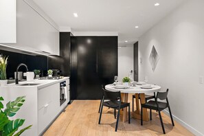 A modern kitchen with a dining area, featuring a round table with chairs, a black cabinet, and a white countertop. - Stylish City 2 Bedroom Gem (Melbourne)