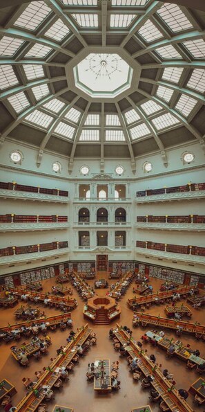 A multi-level library with a central reading area and multiple floors of bookshelves. - Stylish City 2 Bedroom Gem (Melbourne)