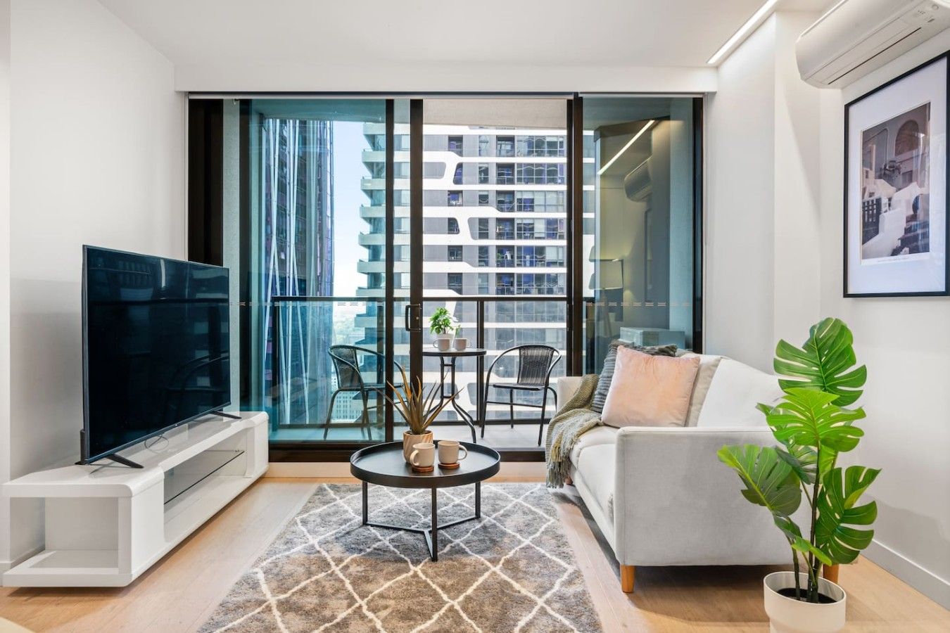 A modern living room with a flat-screen TV, a sofa, a coffee table, and a potted plant.