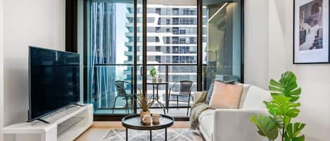 A modern living room with a flat-screen TV, a sofa, a coffee table, and a potted plant.