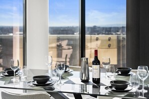 A dining table set for a meal with wine, bowls, and glasses, overlooking a cityscape. - Marvel Penthouse with Pool (Docklands)