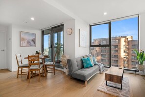 A modern living room with a dining area, large windows, and a view of a building. - Boho Oasis in the City (Melbourne)