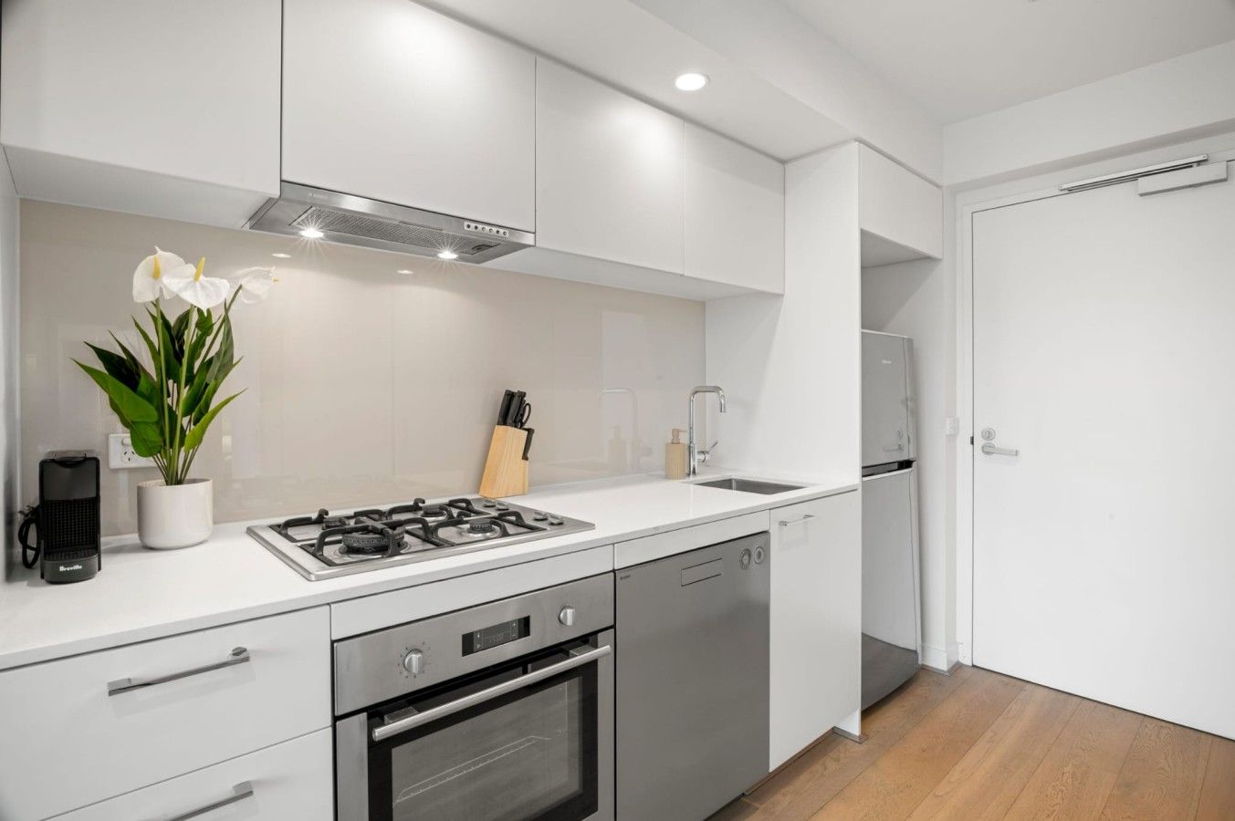 A modern kitchen with white cabinetry, a gas stove, a built-in oven, and a sink.
