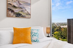 A hotel room with a bed, a painting on the wall, a window with a view, and a lamp. - Boho Oasis in the City (Melbourne)