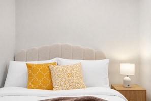 A bed with white bedding and two patterned pillows, a wooden nightstand with a lamp, and a scalloped headboard. - Boho Oasis in the City (Melbourne)