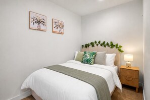 Un dormitorio con cama, mesita de noche, lámpara y dos cuadros con motivos florales en la pared.