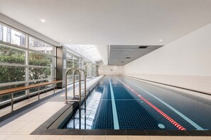 An indoor swimming pool with clear glass walls, metal railings, and a tiled floor. - Zen City Retreat with Parking (Melbourne)