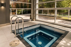 Une piscine intérieure moderne avec des parois en verre transparent, un escalier en métal et un sol carrelé.