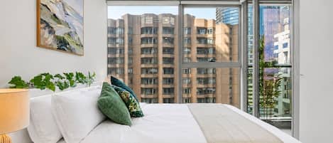 Et hotelværelse med en stor seng, udsigt til skyskrabere og et vindue med udsigt over bybilledet.