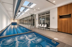 Piscina com vista clara para o teto e janelas, uma receção e uma área de estar com cadeiras.