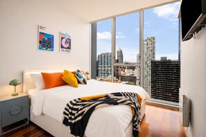 A modern bedroom with a large window, a bed with colorful pillows, and artwork on the wall. - Retro City 3 Bedroom Retreat (Melbourne)