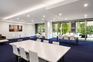 Uma sala de conferência moderna com mesas e cadeiras brancas, janelas amplas e carpete azul.