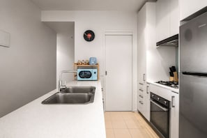 A modern kitchen with a stainless steel sink, a blue microwave, and a stainless steel refrigerator. - Retro City 3 Bedroom Retreat (Melbourne)