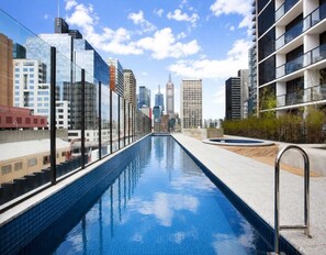 Une piscine sur le toit offrant une vue panoramique sur la ville, entourée d’immeubles modernes.