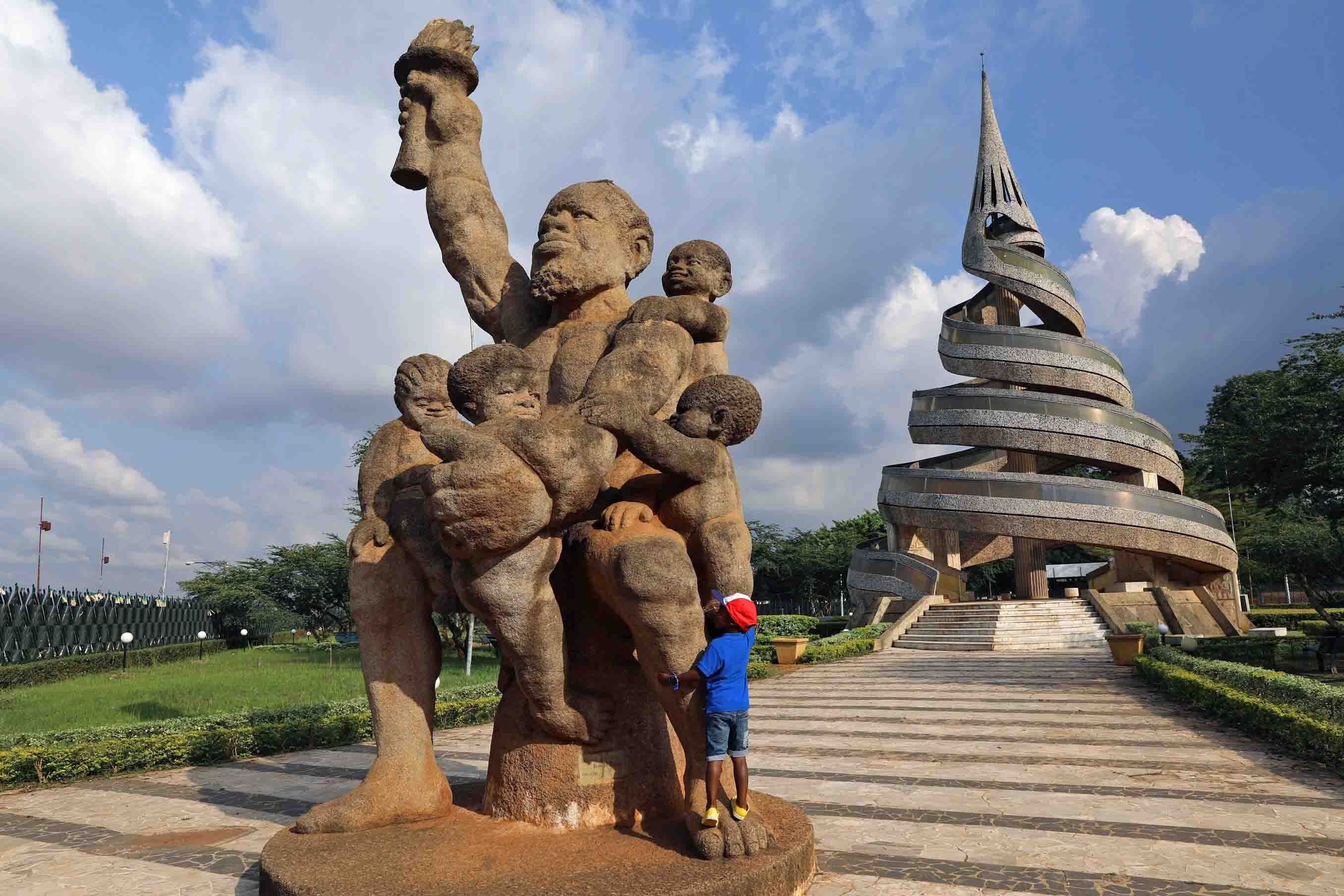 A large stone sculpture of a figure with a child, a spiral tower structure, and a paved pathway.