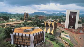 Un edificio moderno con un diseño geométrico singular, rodeado de abundante vegetación y otras construcciones contemporáneas.