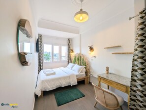 Ett sovrum med en säng, ett skrivbord, en stol, en spegel och ett fönster med gardiner.