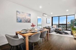 A modern living room with a dining area, large windows, and a cityscape view. - Level 61 City View 3 Bedroom (Melbourne)