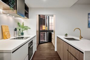 A modern kitchen with white countertops, a built-in oven, and a wooden backsplash. - Level 61 City View 3 Bedroom (Melbourne)