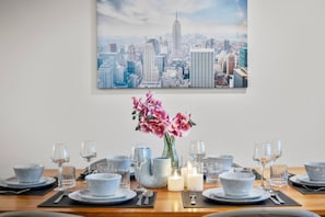 A dining table set with plates, glasses, and cutlery, with a vase of pink flowers in the center. - Level 61 City View 3 Bedroom (Melbourne)