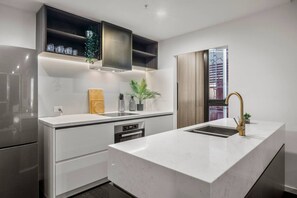 A modern kitchen with a central island, built-in appliances, and a window providing natural light. - Level 61 City View 3 Bedroom (Melbourne)