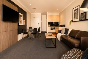 Un salon moderne avec un canapé, une table basse et des fauteuils. Il y a également un coin cuisine équipé de placards et d’appareils électroménagers.