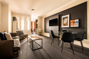 A modern living room with a sofa, coffee table, and a dining area with chairs and a table. - Chinatown 1 Bedroom Apartment (Melbourne)