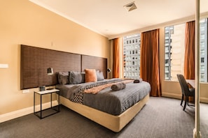 Een moderne hotelkamer met een groot bed, een bureau en uitzicht op hoge gebouwen.