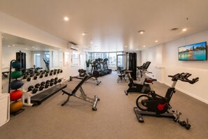A gym with exercise equipment, a mirror, and a city view. - Chinatown 1 Bedroom Apartment (Melbourne)