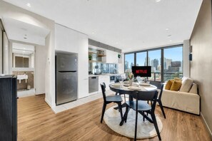 A modern kitchen with a built-in refrigerator, a dining area with a round table and chairs, and a living space with a sofa and a large window offering a city view. - River View Southbank Apartment (Melbourne)