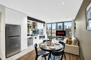 Una cocina moderna con refrigerador empotrado, un comedor con mesa para dos personas y un ventanal que ofrece vistas a la ciudad.