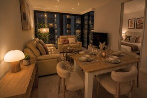 A modern living room with a sofa, a dining table set for four, and a television. - Marvel 2 Bedroom with Balcony (Docklands)