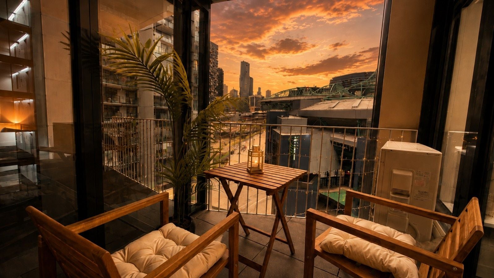A balcony with wooden furniture, a view of the cityscape, and a sunset.