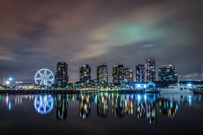 A nighttime cityscape with a prominent Ferris wheel and modern high-rise buildings reflected in calm waters. - Marvel 2 Bedroom with Balcony (Docklands)