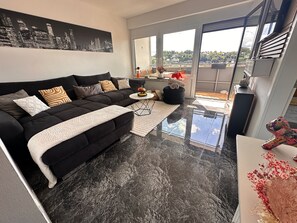 Uma sala de estar moderna com um sofá preto, uma pintura de paisagem urbana e vista através de amplas janelas.