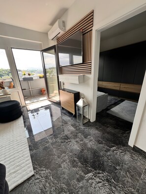 Un intérieur moderne avec une porte vitrée donnant sur un balcon, un bureau intégré et un sol en marbre noir.