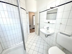 Ein modernes Badezimmer mit weißen Fliesen, einer Badewanne, einem Waschbecken und einer Toilette.