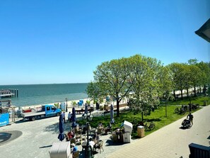 Ein Sitzbereich im Freien mit Tischen und Stühlen, ein Baum und Blick aufs Meer.