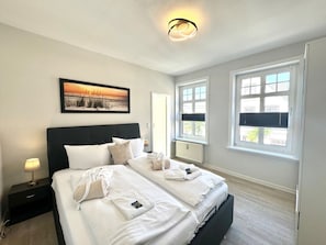 Ein Hotelzimmer mit einem großen Bett, zwei Nachttischen, einem Wandbild und einem Fenster mit Jalousien.