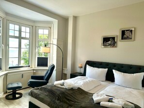 Ein Hotelzimmer mit Bett, Stuhl, Schreibtisch, Lampe und einem Fenster mit Jalousien.