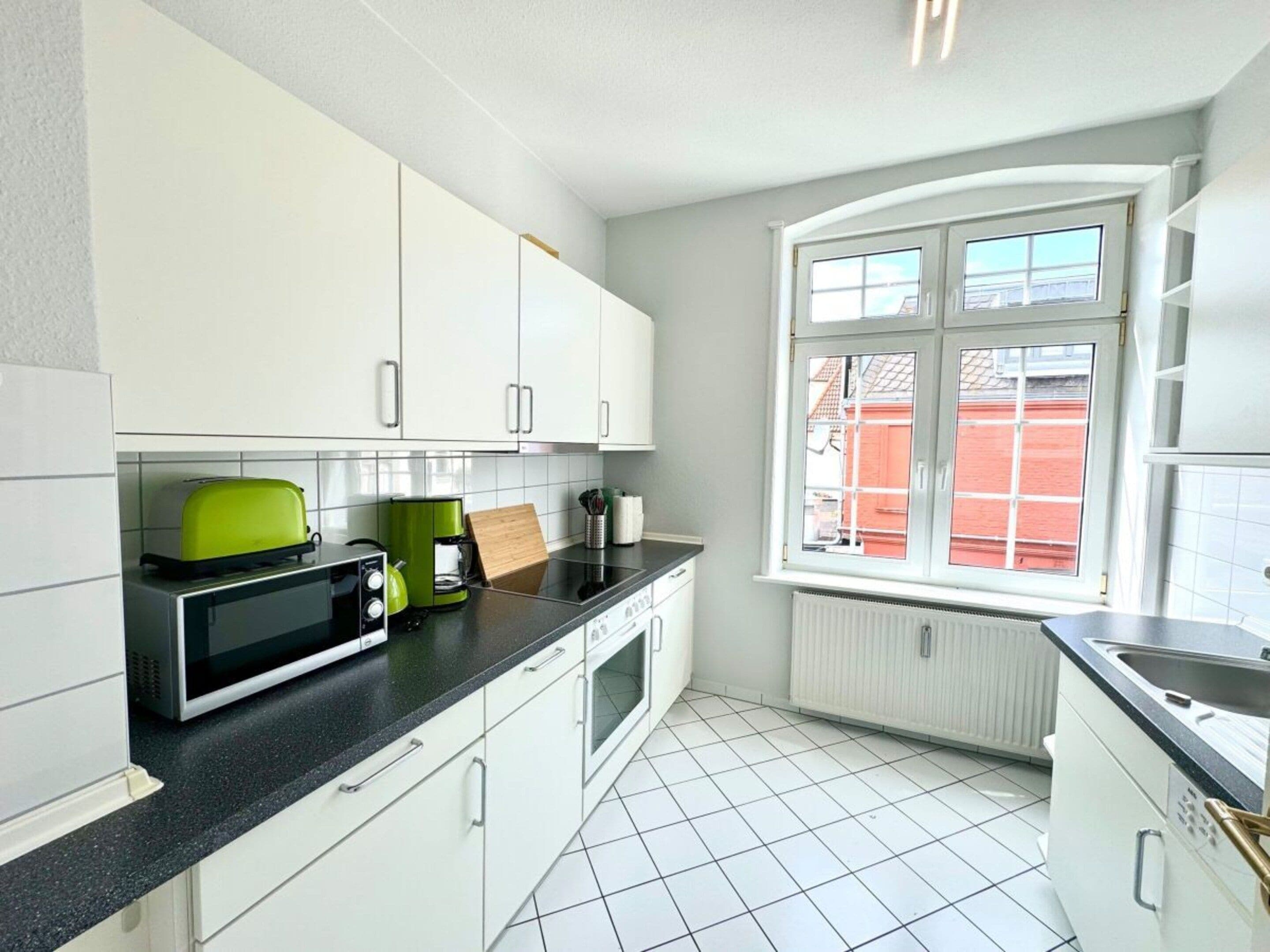 A kitchen with white cabinets, a black countertop, a green toaster, and a window with a view of a red building.