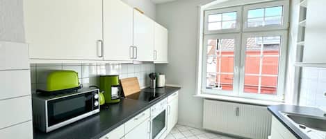 A kitchen with white cabinets, a black countertop, a green toaster, and a window with a view of a red building.