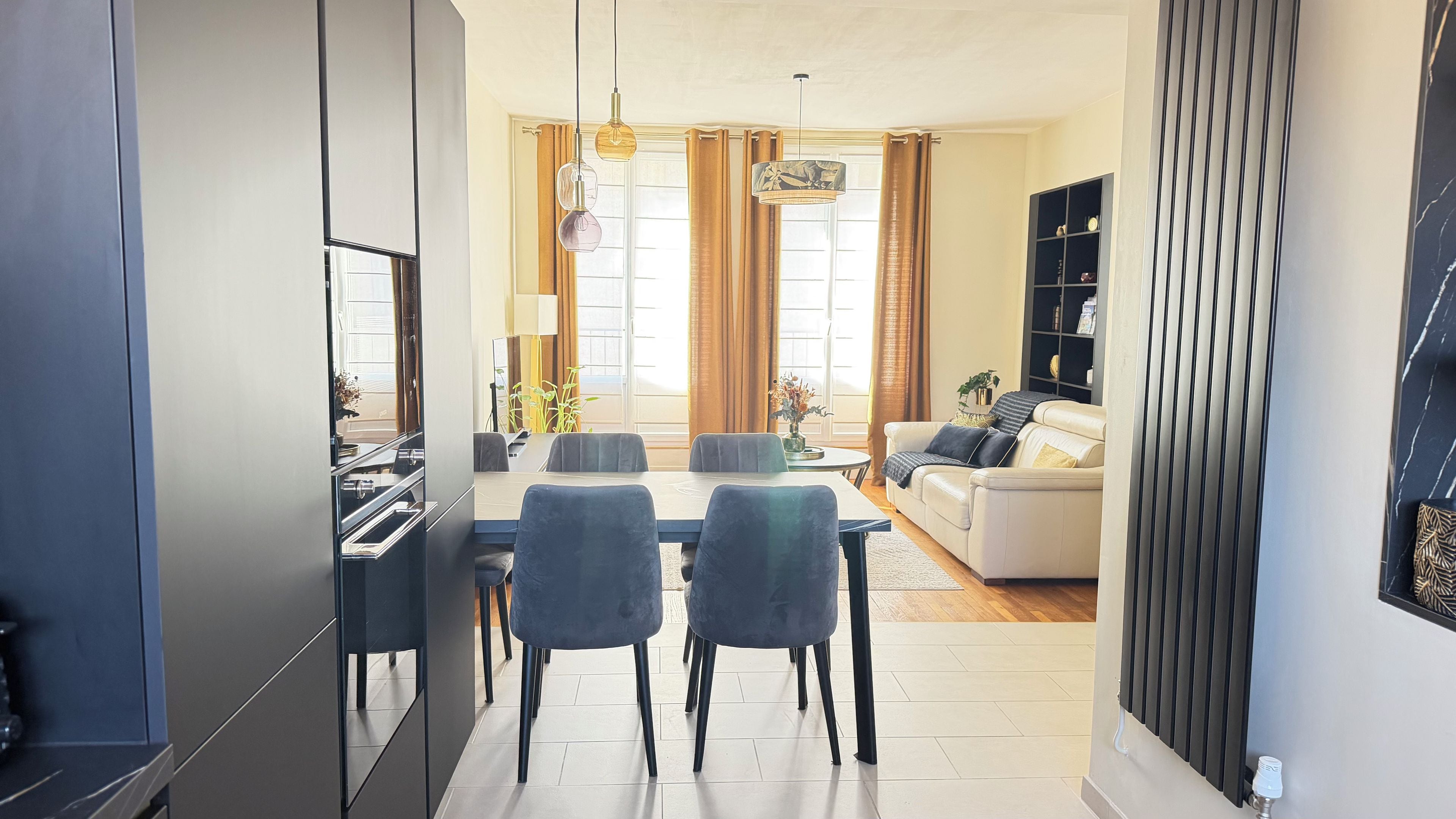 Una sala de estar moderna con un sofá, una mesa de comedor con sillas y una cocina con armarios y un refrigerador.