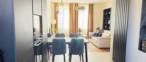 Una sala de estar moderna con un sofá, una mesa de comedor con sillas y una cocina con armarios y un refrigerador.