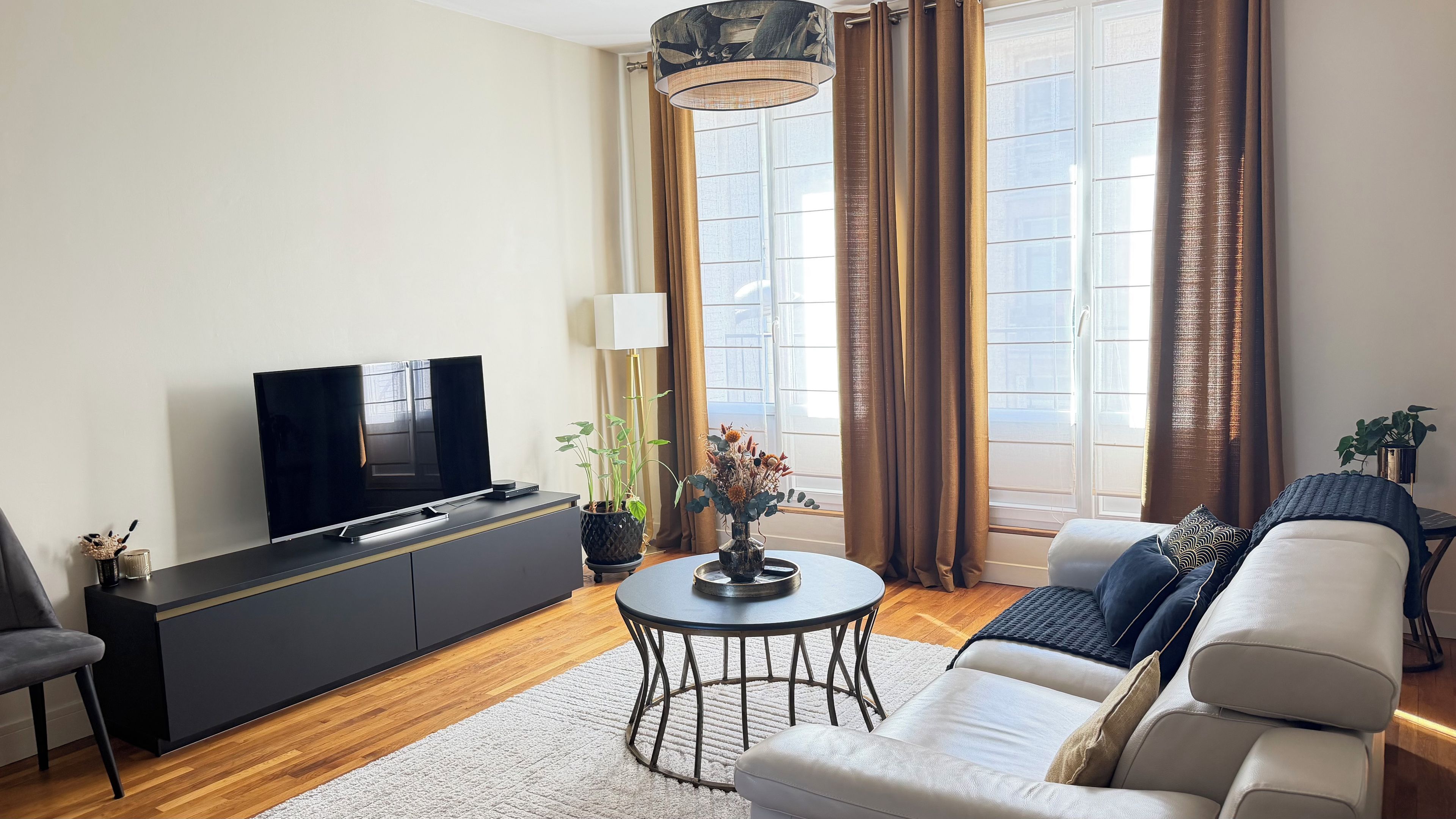 Ein modernes Wohnzimmer mit Flachbildfernseher, einer Couch, einem Couchtisch und einer Topfpflanze.
