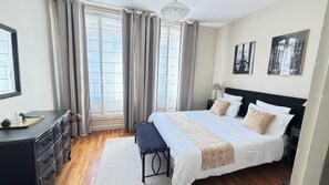 Une chambre d’hôtel avec un grand lit, des tables de chevet, un bureau et une fenêtre avec des rideaux.
