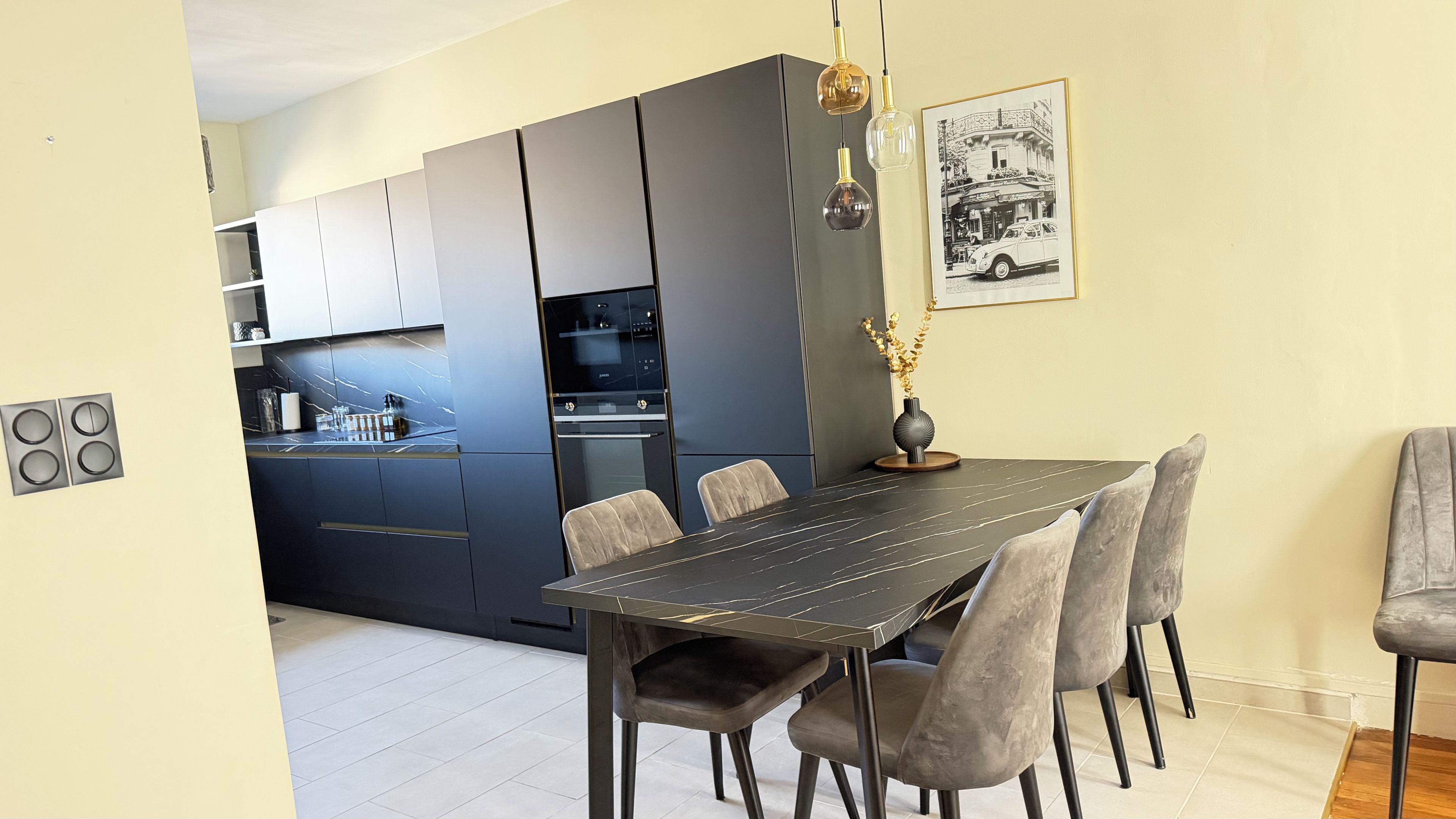 Une cuisine moderne avec des meubles de couleur sombre, une table à manger avec des chaises et un luminaire suspendu.