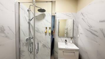 Une salle de bain moderne avec une douche à parois de verre, un lavabo blanc et un mur recouvert de carreaux de marbre.