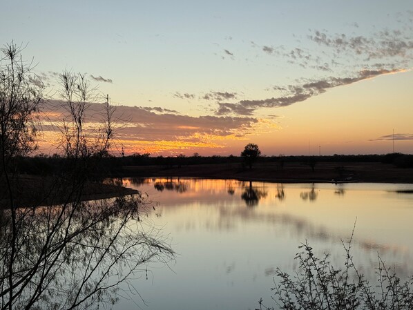 A calm body of water reflecting the sky, surrounded by sparse vegetation and a distant tree line.