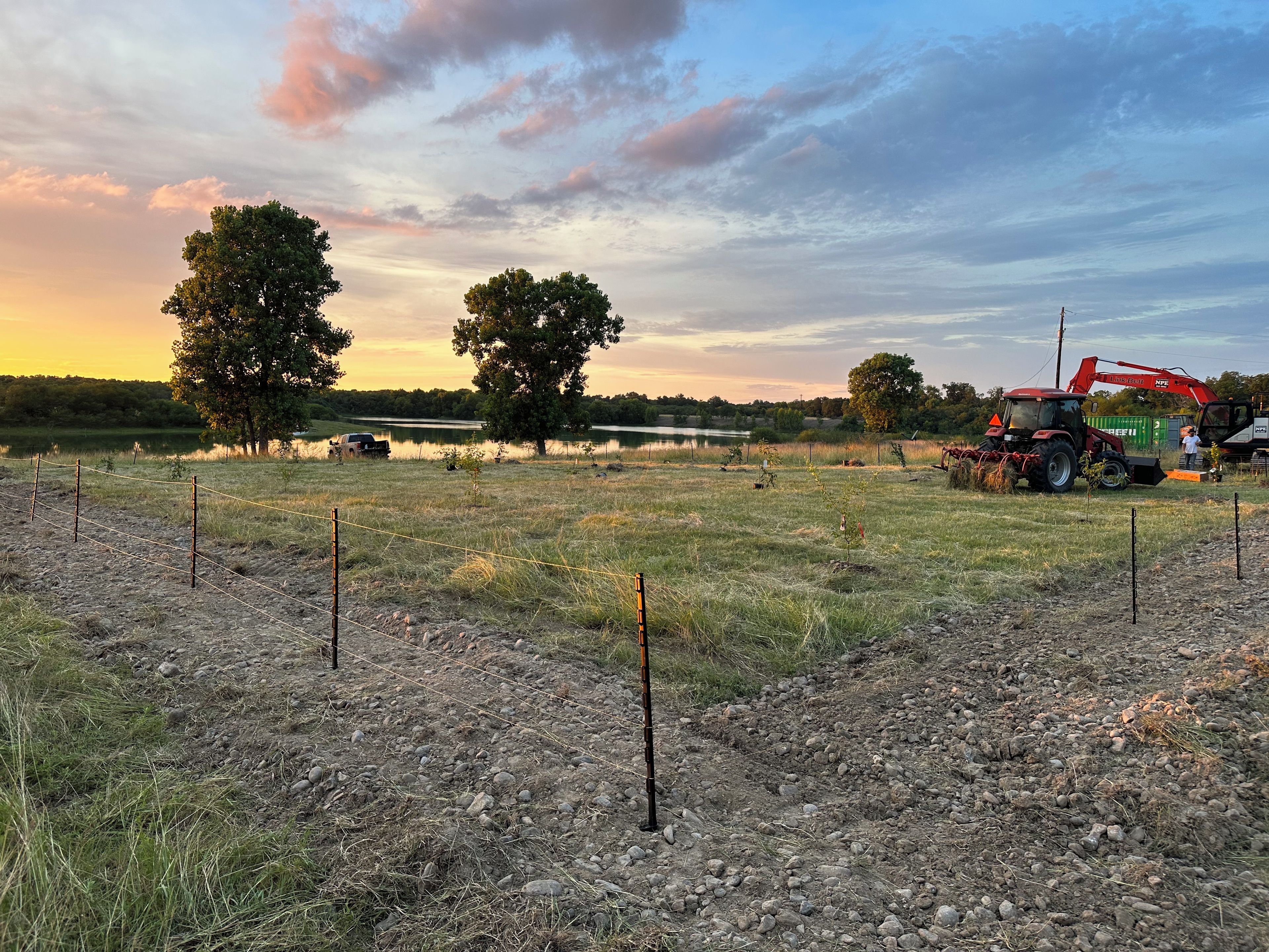 Un paysage rural avec un tracteur et une remorque, une zone délimitée par une clôture et des arbres.